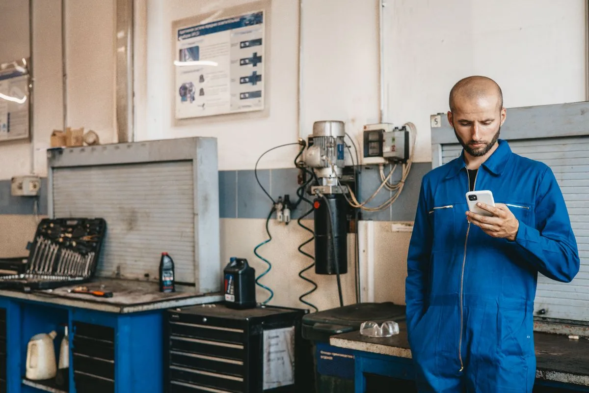 Mecânico de uniforme olhando o celular na oficina