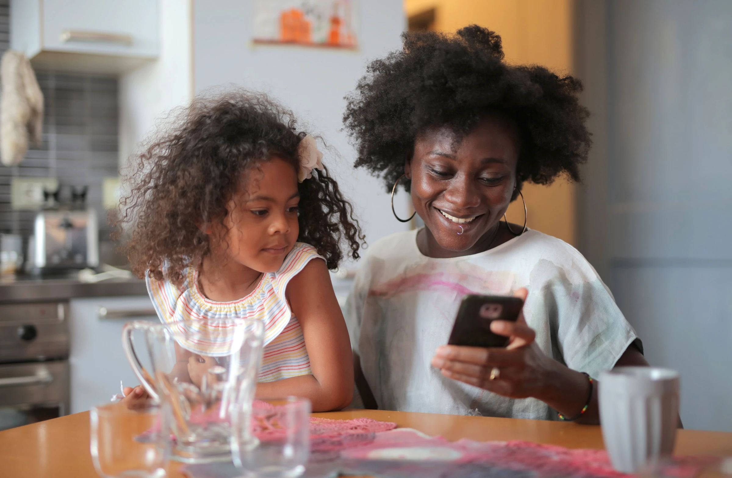 Mãe e filha na mesa da cozinha olhando o celular